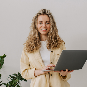 White woman in yellow shirt carrying a laptop as part of an online check in session